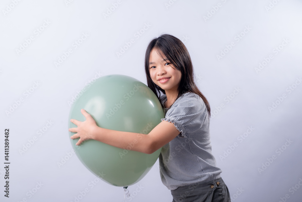 Asian girl with long black hair smiles while hugging a large round green balloon, wearing a striped blouse and dark skirt, standing sideways indoors against a clean white studio background Asian girl with long black hair smiles while hugging a large round green balloon, wearing a striped blouse and dark skirt, standing sideways indoors against a clean white studio background