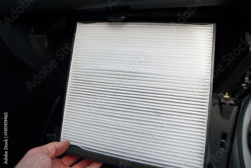 Obraz na płótnie Hand with new clean cabin air filter, ready to install inside the glovebox of car as part of routine maintenance to improve air quality, ventilation. New cabin air filter installation. Selective focus w salonie