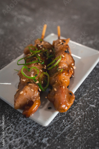 Two chicken yakitori skewers garnished with sesame seeds and scallions on white plate