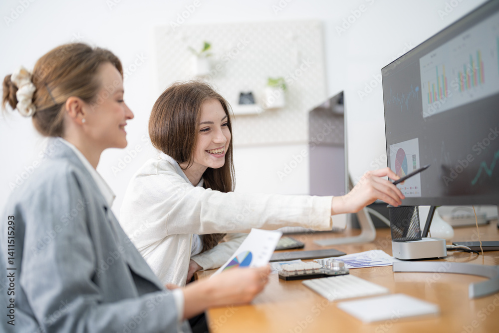 Two women collaborating in a modern office while analyzing graphs on a computer screen and discussing data insights Two women collaborating in a modern office while analyzing graphs on a computer screen and discussing data insights