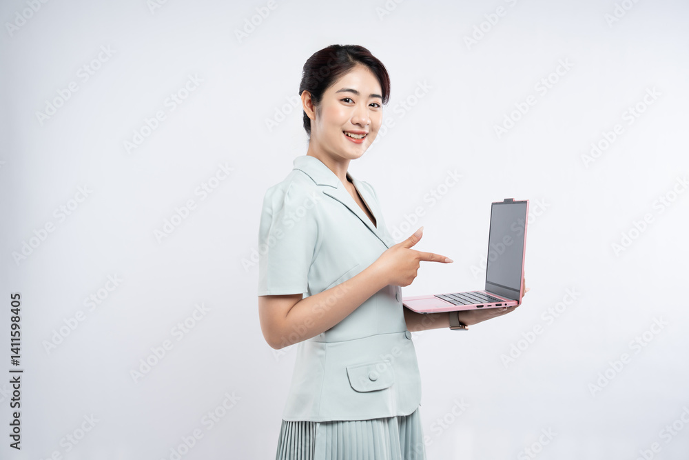 Smiling woman in pastel suit presents a pink laptop gesturing towards the screen on a white backdrop Smiling woman in pastel suit presents a pink laptop gesturing towards the screen on a white backdrop