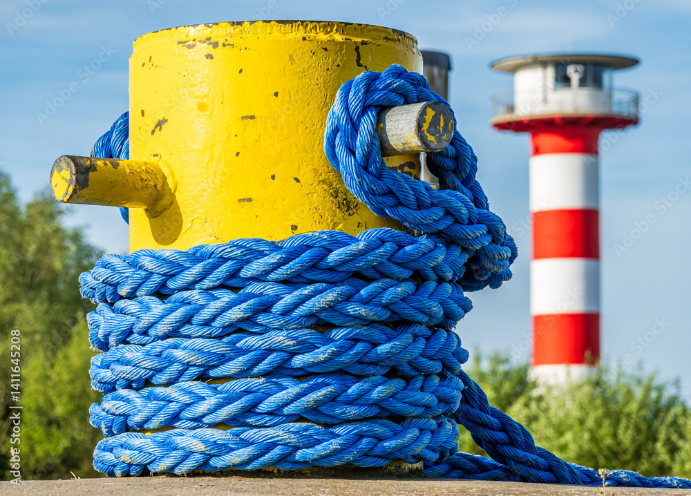 Colorful mooring post with blue rope and a striped lighthouse in the background against a clear sky in a coastal location
