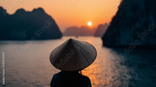 Person in traditional hat gazes at serene sunset over water, ideal for travel or culture themes