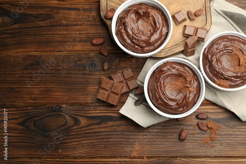 Obraz na płótnie Tasty pudding in bowls, pieces of chocolate and cocoa beans on wooden table, flat lay. Space for text w salonie