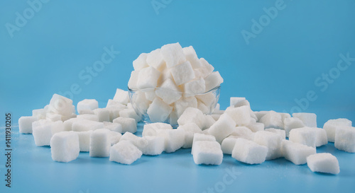 Photos White sugar in a glass cup, scattered lump sugar on a blue background