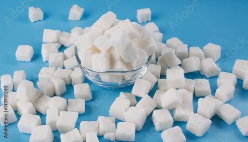 Foto White sugar in a glass cup, scattered lump sugar on a blue background