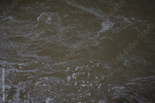 Fotografie A foamy, murky river flows through a rocky landscape