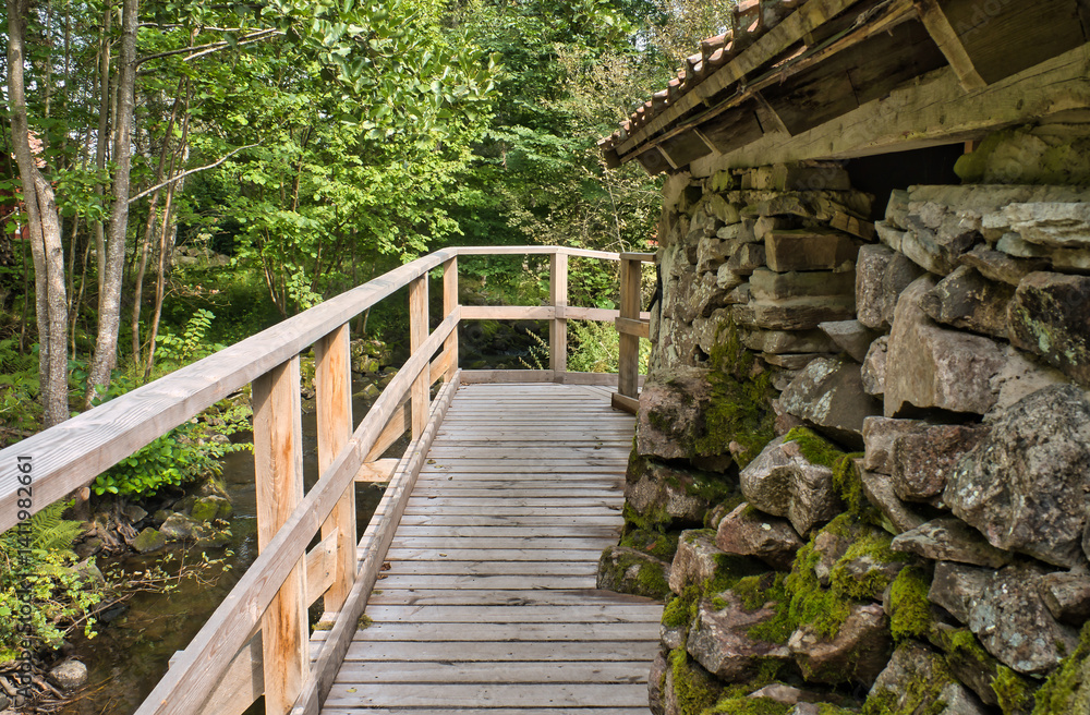 Fototapeta premium Old watermill surrounded by green nature. Moss-covered stones, surrounded by trees.