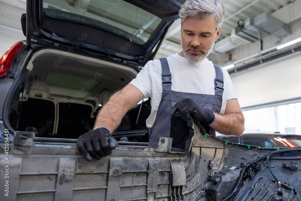 Bearded automotive worker in workshop performing diagnostics and inspection on transport vehicle Bearded automotive worker in workshop performing diagnostics and inspection on transport vehicle
