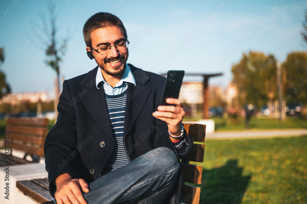 Fototapeta premium Business professional man smiling during a video chat on his smart device while relaxing at the city park.