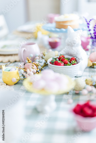 Easter table set up pink cups and bunny statue holding strawberries