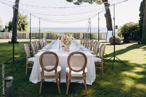 wedding. A festive table adorned with flowers and candles stands on a green meadow among the trees, with a view of the sea and the sky