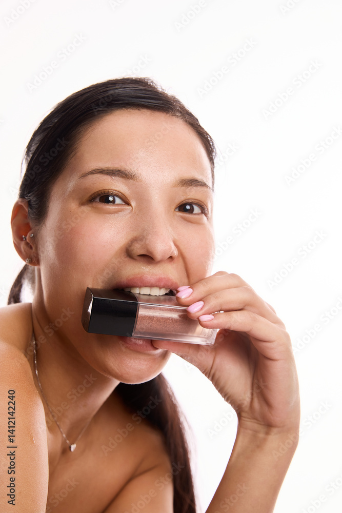 Young Korean woman with clean skin, without makeup holding makeup bottle near lips, expressing playful elegance and modern skincare routine. Concept of beauty, cosmetics and cosmetology