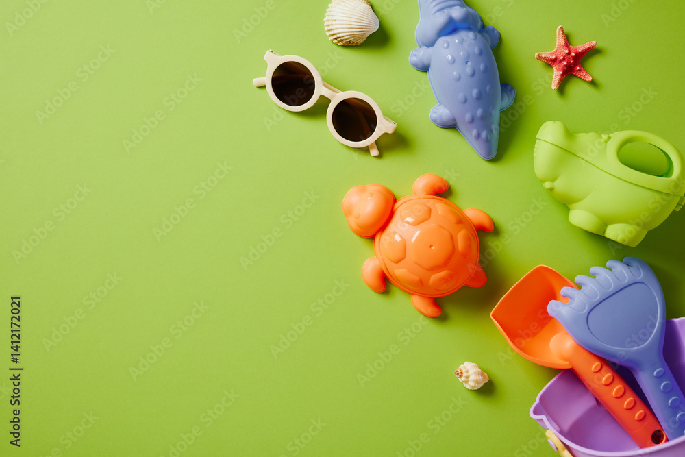 Various kids beach toys like sunglasses, pail, shovel, molds, shells flat lay on green surface with copy space. Various kids beach toys like sunglasses, pail, shovel, molds, shells flat lay on green surface with copy space.