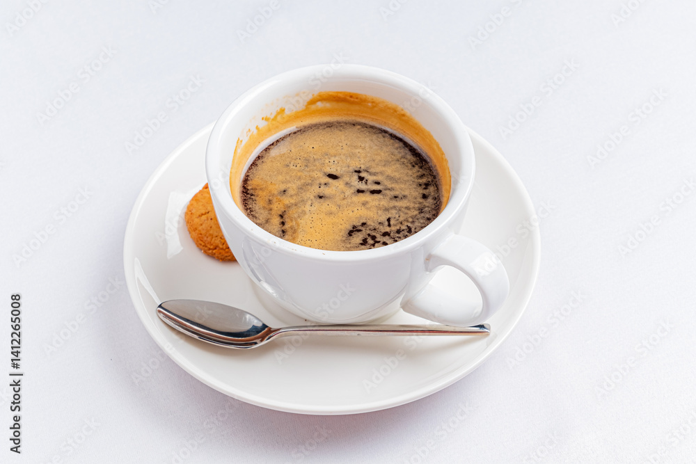A steaming cup of coffee sits elegantly on a white saucer alongside a sweet cookie
