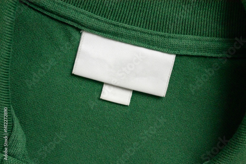 Blank white laundry care clothes label on green shirt fabric texture background