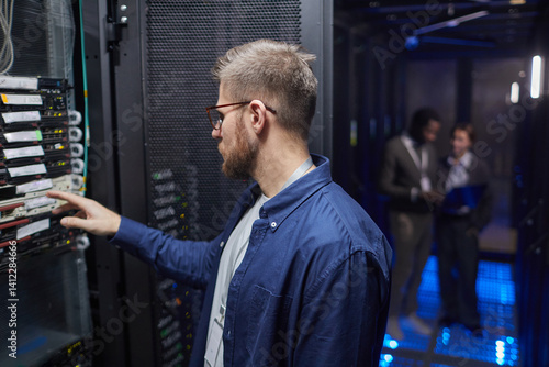 Tableau sur toile Technician in blue shirt configuring server rack in data center with colleagues in background