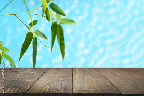 Empty wooden table top against blurred summer background with bamboo leaves and blue water. Space for design. Composition for various design concepts.
