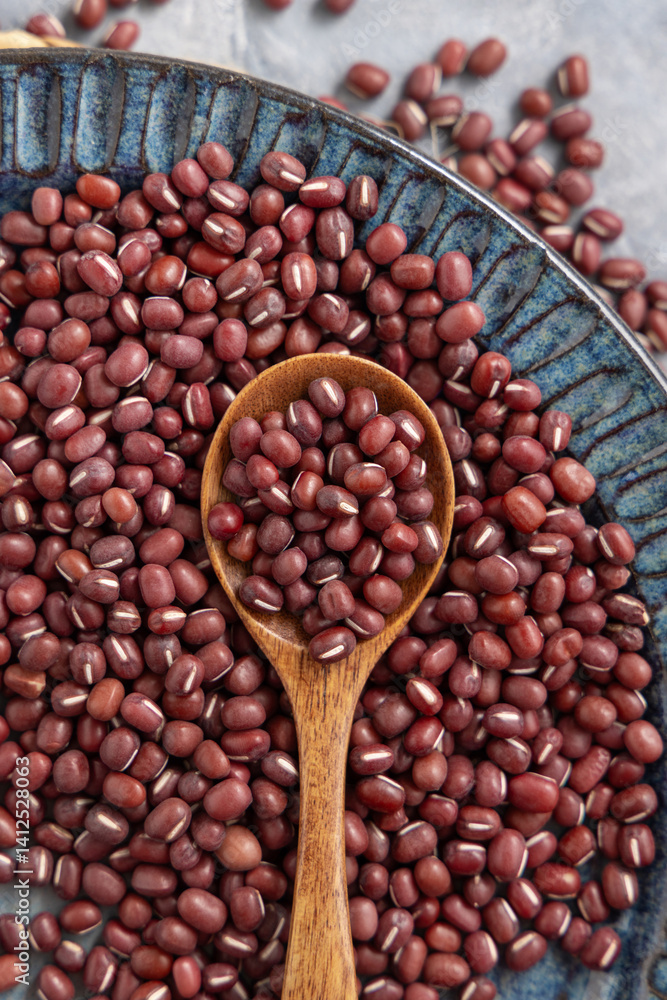 Blue plate full of dried red azuki beans with a wooden spoon top view. Vegetarian protein source