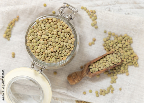 Obraz na płótnie Glass jar full of raw green lentils with a wooden scoop on white table top view. Dried legumes w salonie