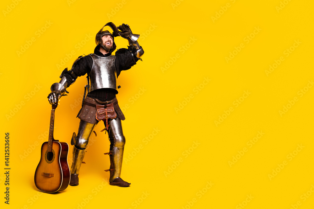 Young man dressed in medieval knight armor with guitar on vibrant yellow background Young man dressed in medieval knight armor with guitar on vibrant yellow background