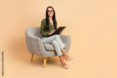 Confident businesswoman with clipboard sitting on beige background, showcasing professionalism and poised demeanor in modern office attire