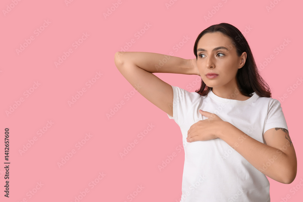 Young woman checking her breast on pink background. Cancer awareness concept