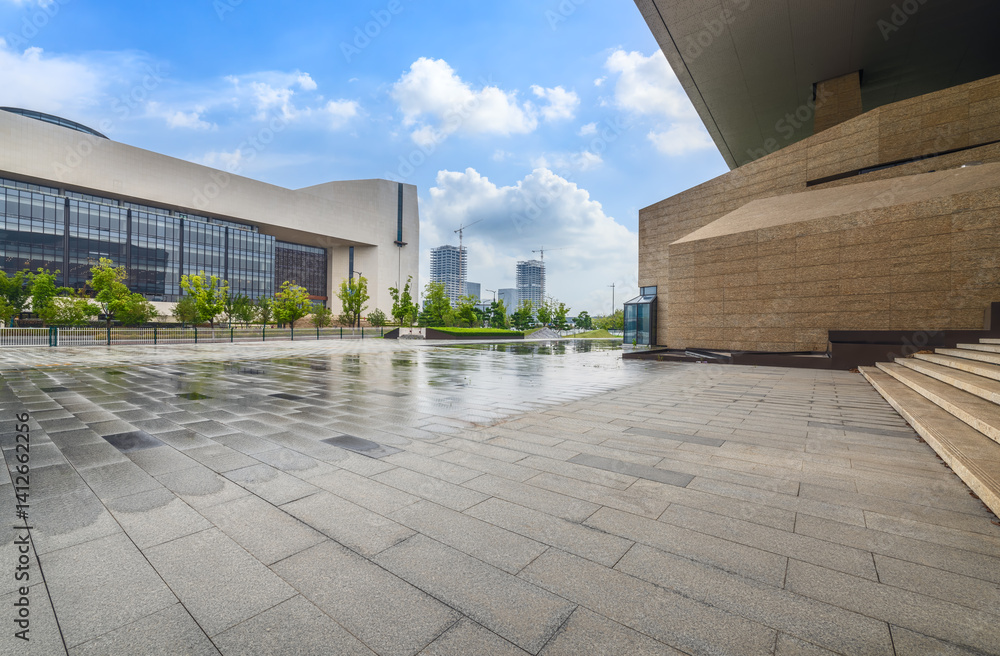 Obraz premium Wet empty stone floor pavement and modern office building exterior in city.