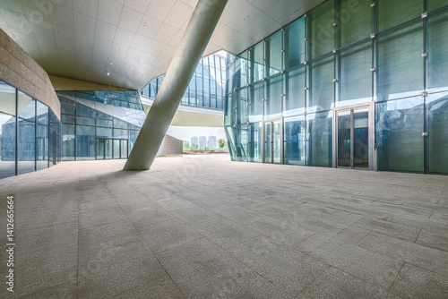 Empty stone floor within modern architecture building featuring glass walls large pillar and open plaza background.