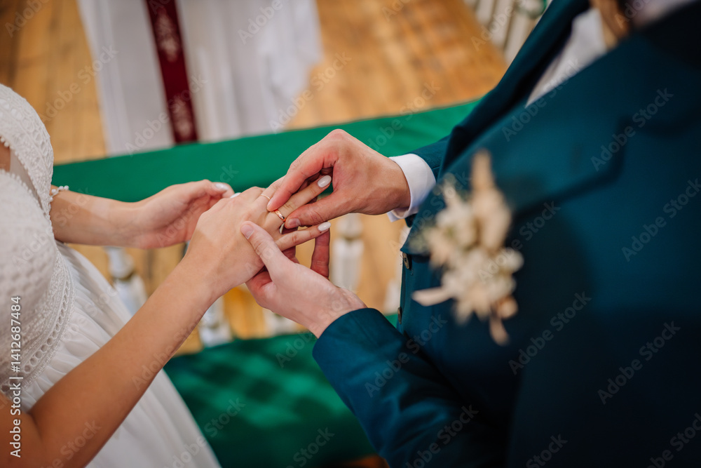 Fototapeta premium Close-up of groom placing a wedding ring on the bride’s finger during the ceremony, symbolizing love, unity, and commitment..