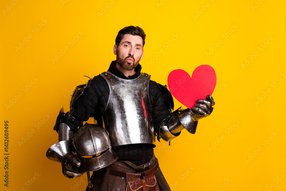 Obraz premium Handsome man in medieval knight armor holding a red heart symbol on yellow background