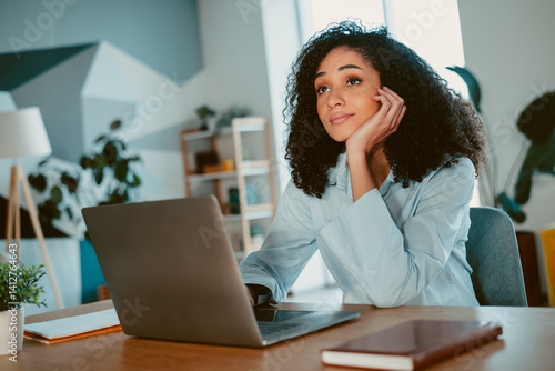 Quadro em tela Young woman indoors daydreaming at a laptop while seated in a cozy modern worksp
