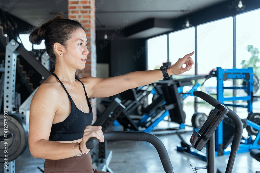 Fototapeta premium Young woman exercising in a gym while using an elliptical machine during a sunny afternoon