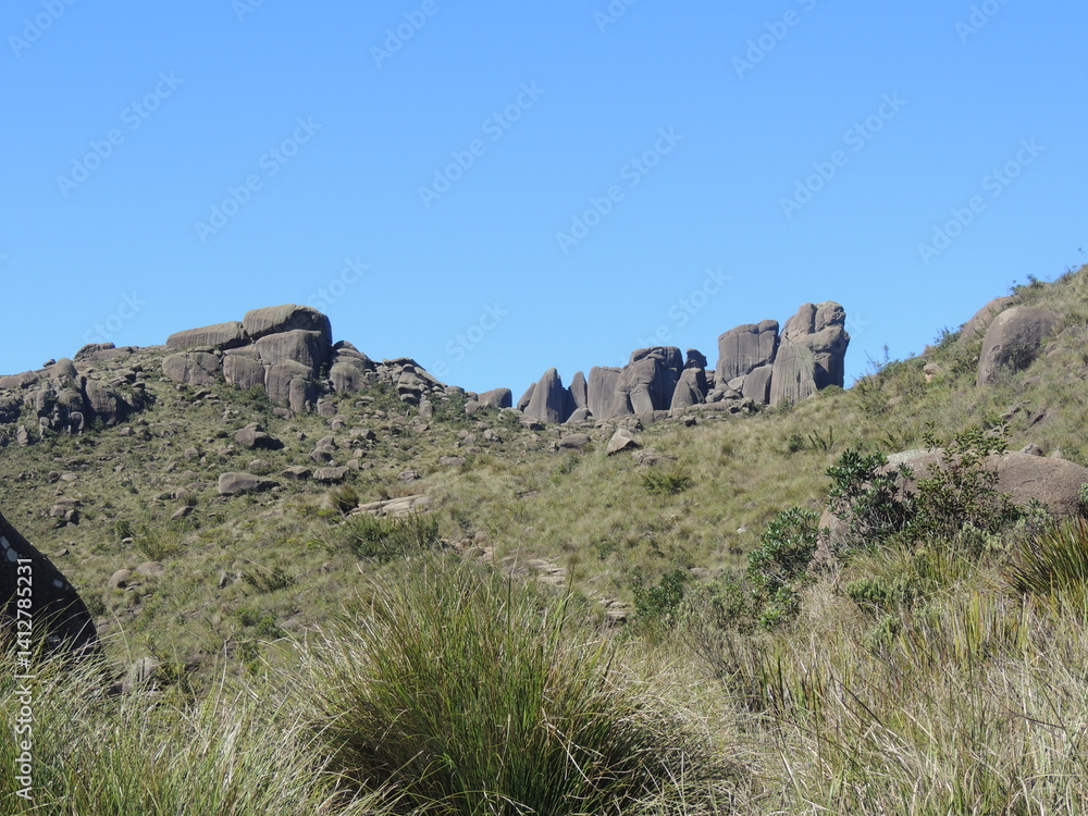 Imposing rock formation rises above a rugged mountain landscape under a clear blue sky, evoking timeless natural strength and mystery. Imposing rock formation rises above a rugged mountain landscape under a clear blue sky, evoking timeless natural strength and mystery.