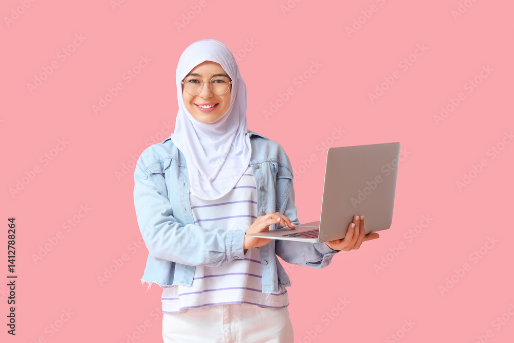 Beautiful young Muslim woman in hijab with modern laptop on pink background Beautiful young Muslim woman in hijab with modern laptop on pink background