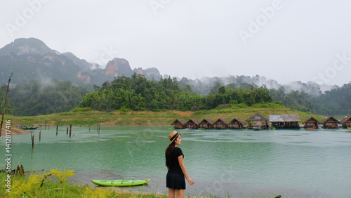 Obraz na płótnie woman stands by serene lake with floating huts and misty mountains in background, creating peaceful scene w salonie