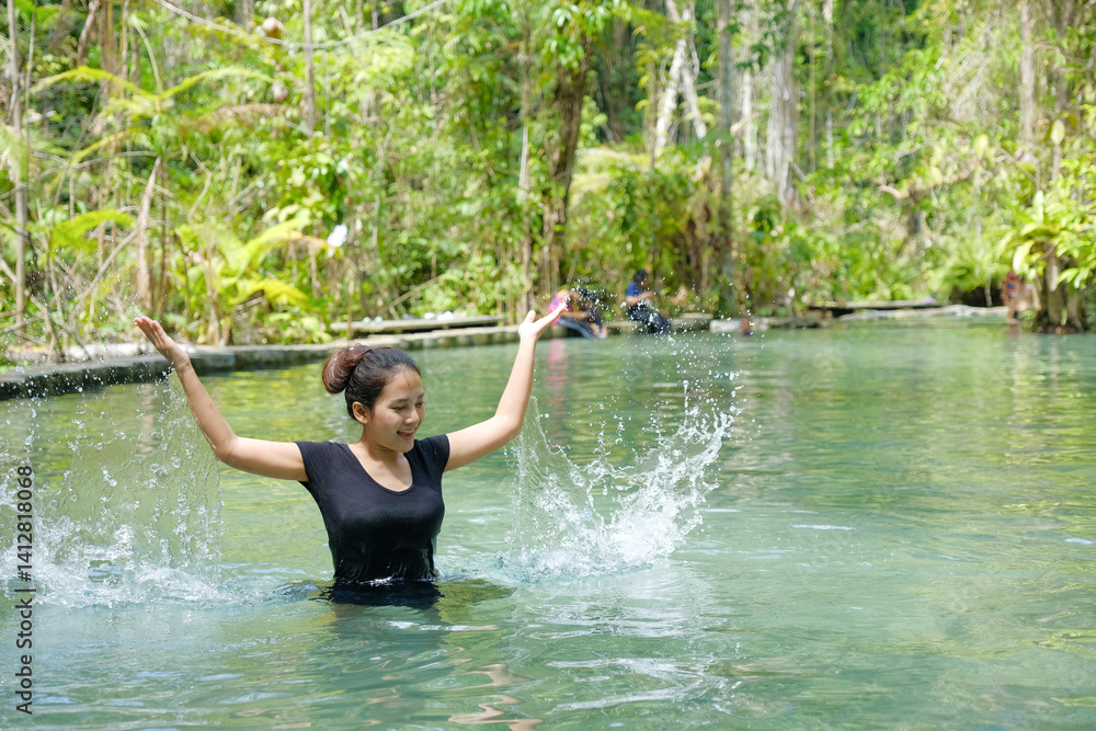 woman joyfully splashes water in lush, tropical river surrounded by greenery