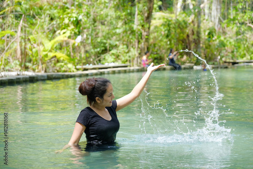 Obraz na płótnie woman in black shirt joyfully splashes water in serene natural pool surrounded by lush greenery w salonie