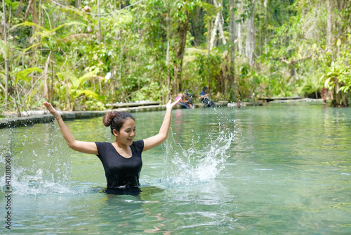 woman joyfully splashes water in lush, tropical river surrounded by greenery