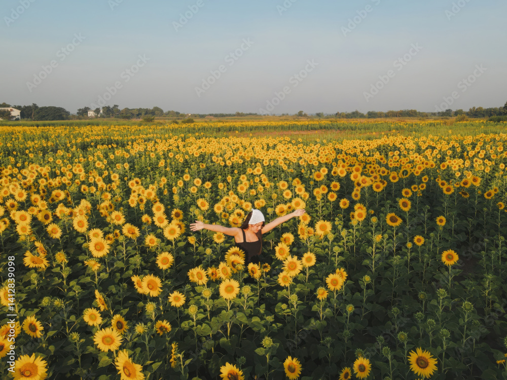 person joyfully stands in vast sunflower field under clear blue sky, arms outstretched in happiness