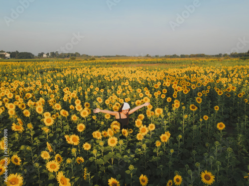 person joyfully stands in vast sunflower field under clear blue sky, arms outstretched in happiness