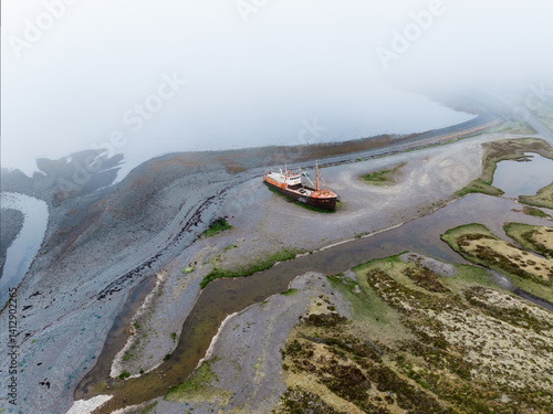 Obraz na płótnie Aerial view of a rusted shipwreck stranded on a misty Icelandic shore. Surrounded by wetlands and tidal patterns, the abandoned vessel adds mystery to the remote coastal landscape. w salonie