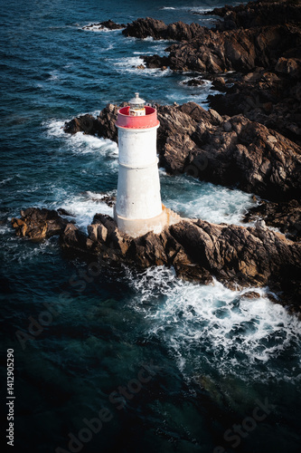 Obraz na płótnie Aerial view of the lighthouse at Capo Ferro, Sardinia, standing on rugged rocks surrounded by deep blue sea and crashing waves. A dramatic coastal landmark in the Mediterranean. w salonie