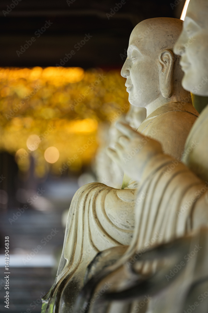 Close-up of serene Buddha statues in a temple corridor, with soft golden bokeh in the background. The composition evokes calm, mindfulness, and spiritual presence in a sacred space.