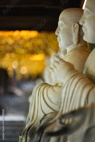 Obraz na płótnie Close-up of serene Buddha statues in a temple corridor, with soft golden bokeh in the background. The composition evokes calm, mindfulness, and spiritual presence in a sacred space. w salonie