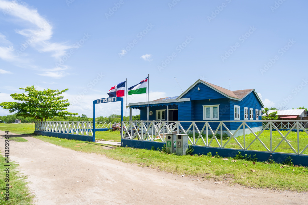 Blue wooden building is a police station in a small village, fenced by a low wooden fence and the flag of the Dominican Republic on the roof,Saona island, Mano Juan village.