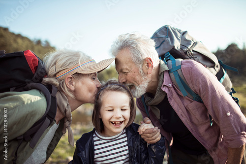 Happy grandparents kissing granddaughter during outdoor hiking trip