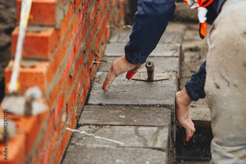 Mason laying concrete blocks while constructing retaining wall at construction site