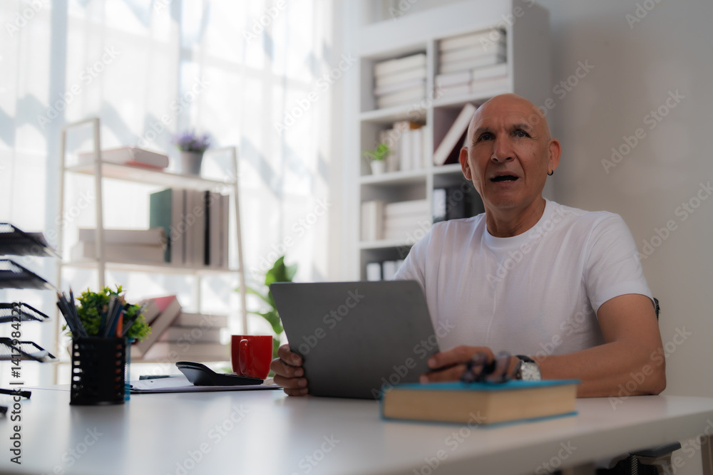Surprised senior manager is working with a laptop at his desk in a bright, modern office, holding his glasses and looking up with an expression of amazement Surprised senior manager is working with a laptop at his desk in a bright, modern office, holding his glasses and looking up with an expression of amazement