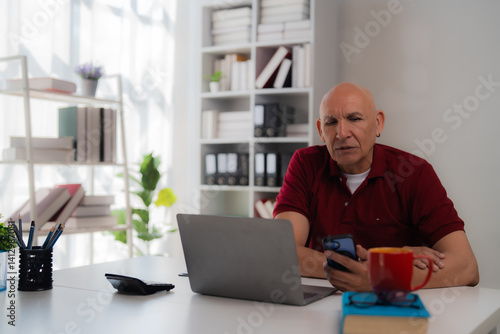 Wallpaper Mural Focused mature businessman using laptop and smartphone while sitting at desk in bright modern office, managing business and working remotely Torontodigital.ca
